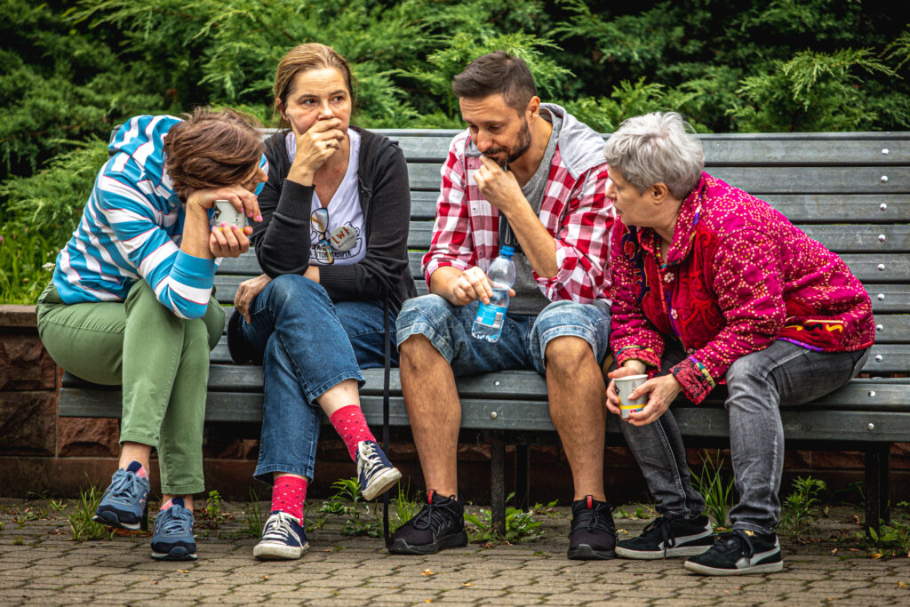 Zdjęcie. Czwórka prowadzących zajęcia podczas Lata w Teatrze rozmawia siedząc na ławce.