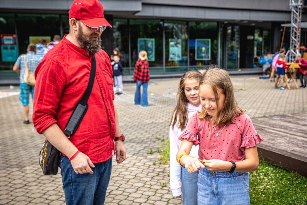 Zdjęcie. Przemek Krystian przygląda się, jak dziewczynka zaplata na nadgarstku właśnie otrzymany odblask-bransoletkę.