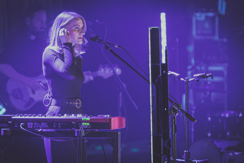 Zdjęcie. Kaśka Sochacka stoi za keyboardem. Prawą ręką poprawia sobie włosy. Scena skąpana w fioletowym świetle scenicznym.