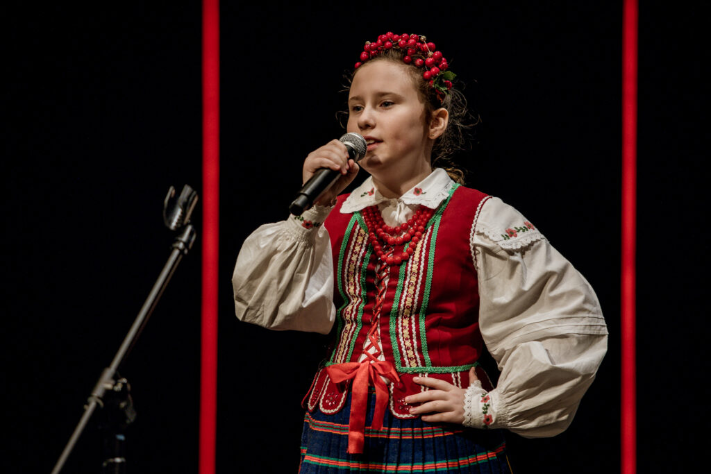 Zdjęcie. Mała dziewczyna śpiewa do mikrofonu. To uczestniczka konkursu wokalnego im. Jopka.