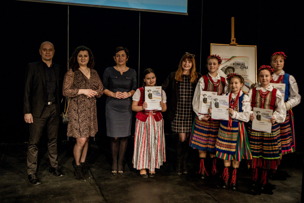 Zdjęcie. Pięć dziewczynek w strojach ludowych prezentuje dyplomy konkursu Jopka, organizowanego co roku przez Mazowsze. Obok jury eliminacji wojewódzkich: m.ni. Augustyna Nowacka i Tomasz Kot.