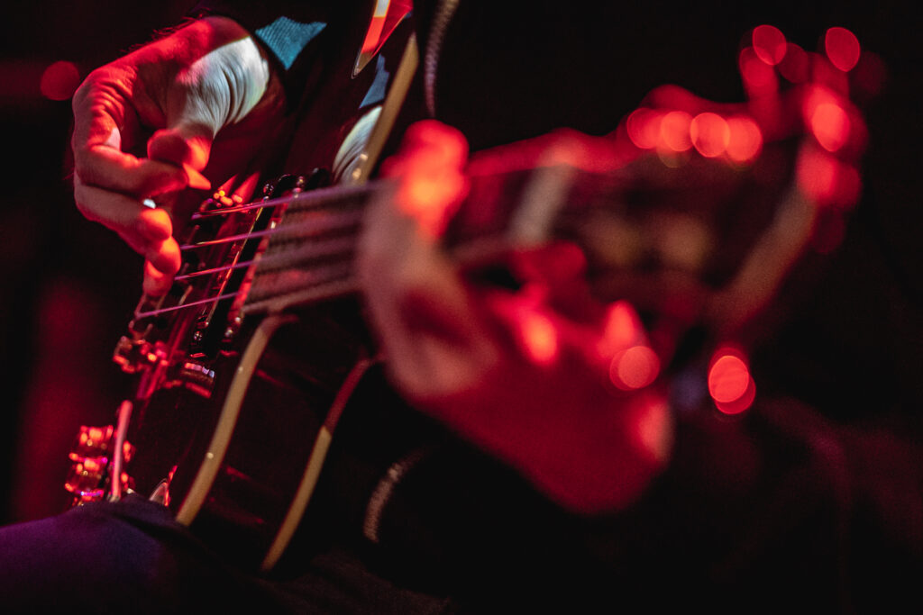 Gitara, na której ktoś gra. Scena oświetlona różowym światłem.