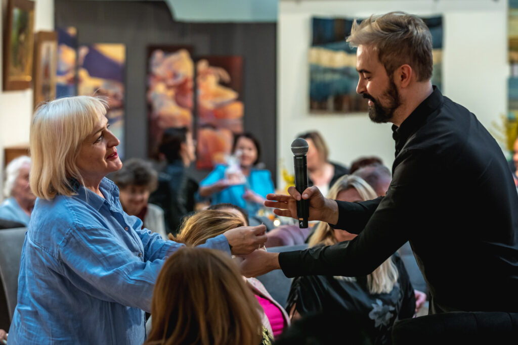 Zdjęcie. Salon Kobiet Wicedyrektor Artur Wijata wręcza książkę blondynce z widowni.