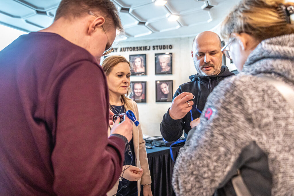 Zdjęcie. Hol przed wejściem nad Małą Scenę KCK. Pracownicy KCK rozdają odbiorniki do audiodeskrypcji.