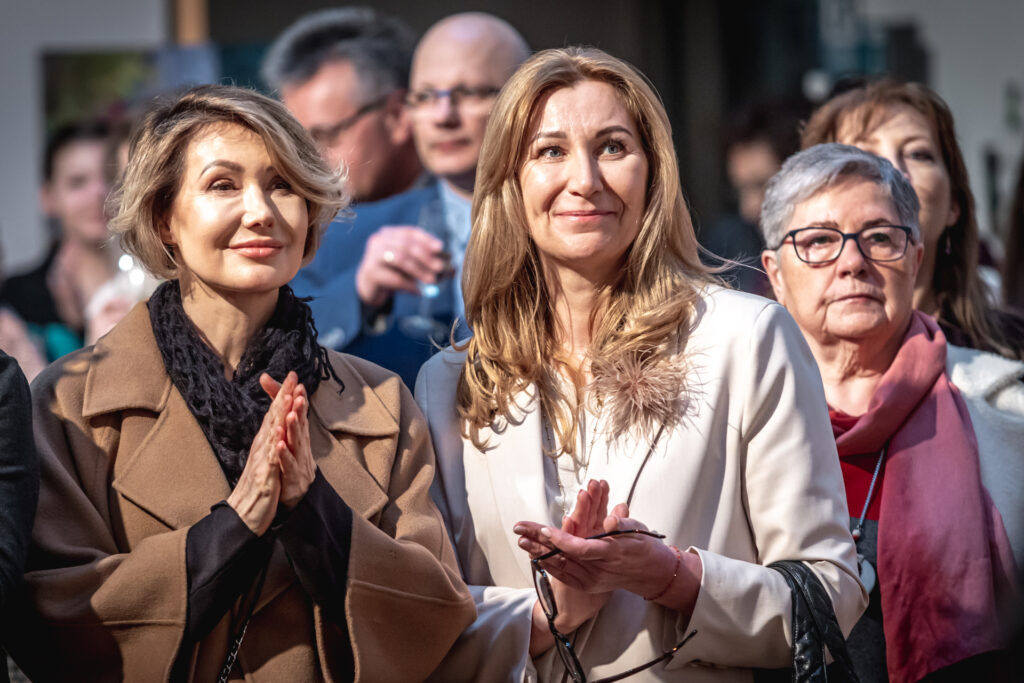 Zdjęcie. Publiczność wernisażu w galerii "Winda". Trzy panie patrzą w jednym kierunku, zadzierając wzrok do góry, Uśmiechają się