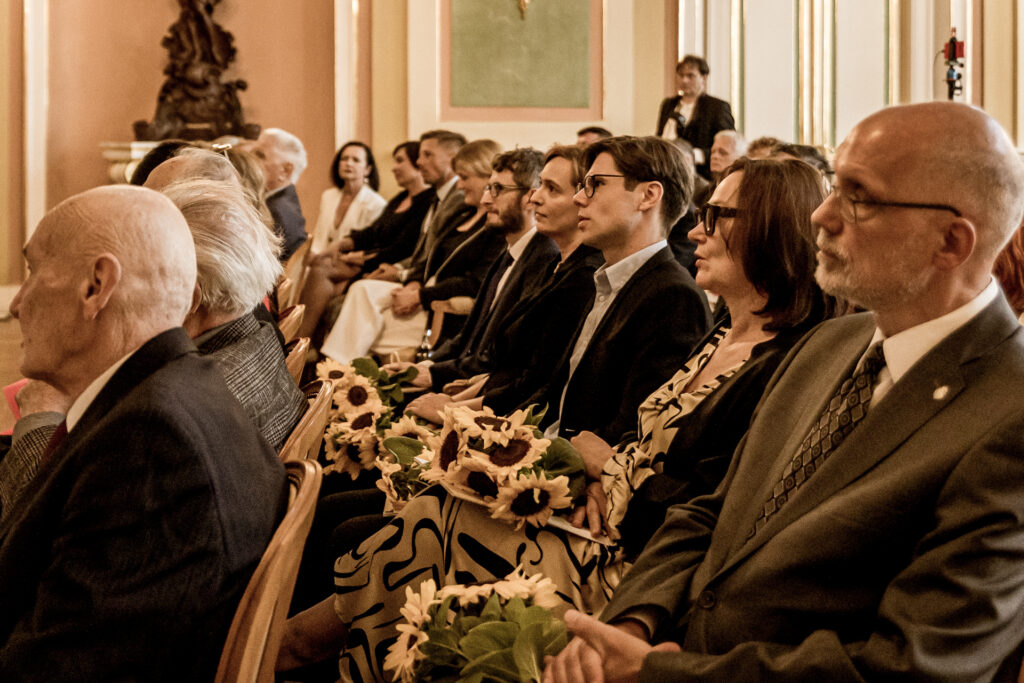 Zjdęcie. Publiczność ogłoszenia nominacji do tytułu Mistrza Mowy Polskiej. Wszyscy siedzą na fotelach i patrzą w jednym kierunku.