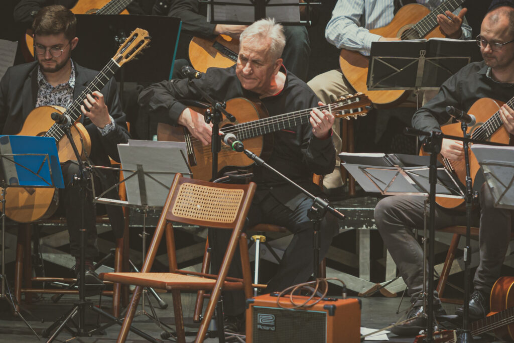 Zdjęcie. Jerzy Pikor gra na gitarze. Obok inni muzycy.