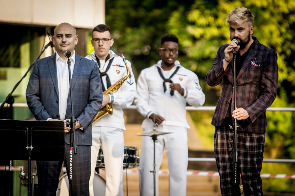 Zdjęcie. Wicedyrektor KCK Artur Wijata i konsul Erjon Kruja, z Konsulatu Generalnego USA w Krakowie, zapowiadają koncert zespołu TopSide Band.