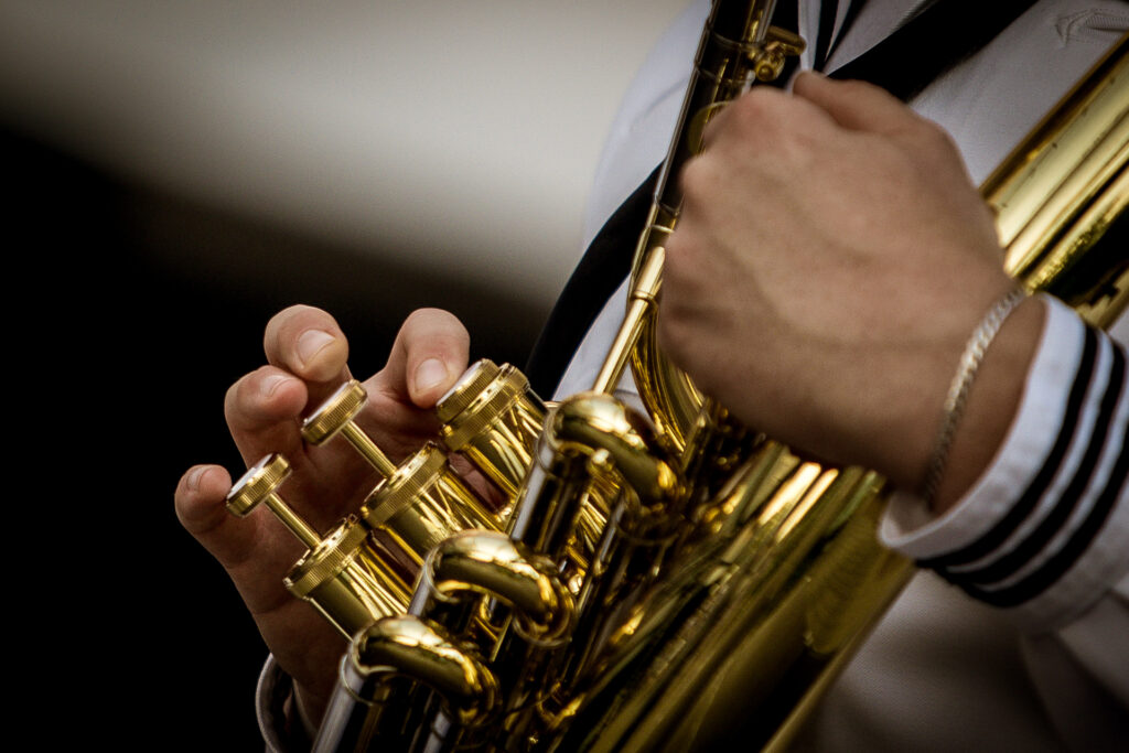 Zdjęcie. Zbliżenie. Dłonie na przyciskach złotego instrumentu dętego.