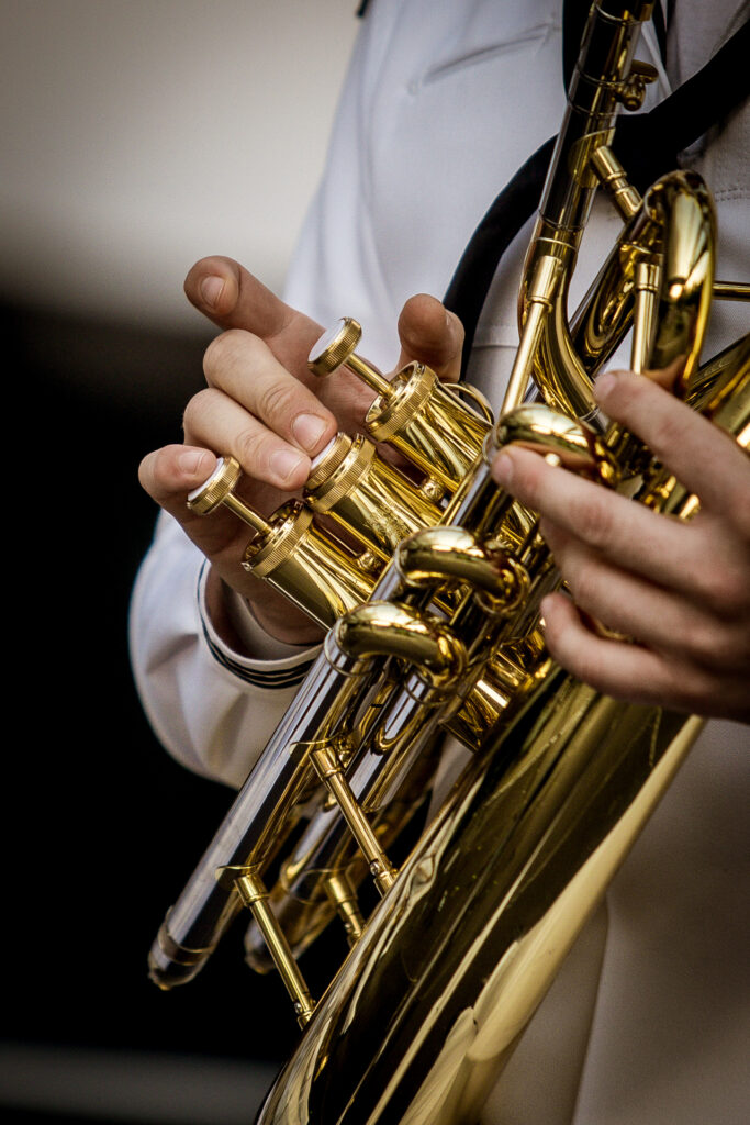 Zdjęcie. Zbliżenie. Dłonie na przyciskach złotego instrumentu dętego.