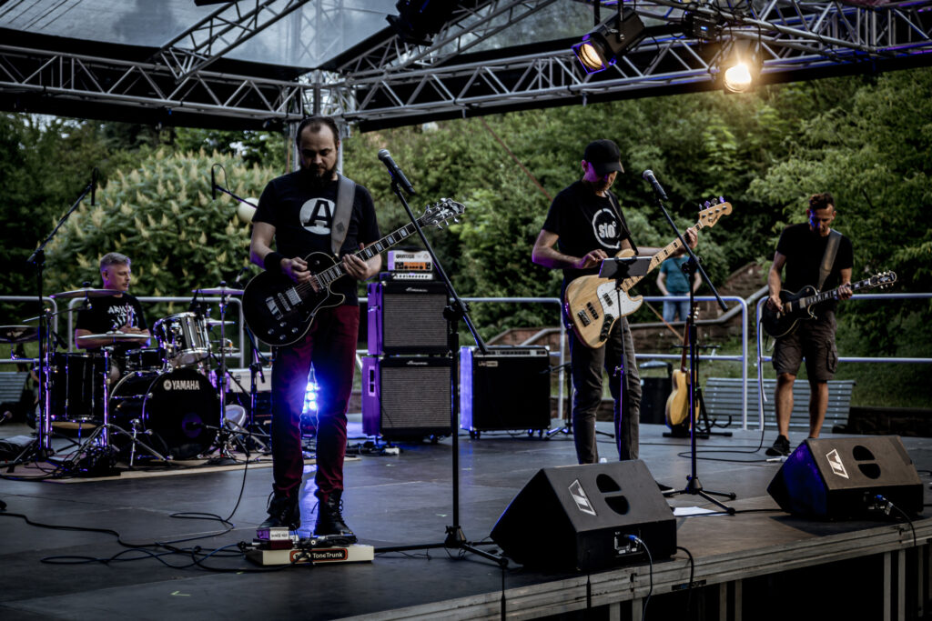 Zdjęcie. Czterech muzyków na scenie letniej Keleckiego Centrum Kultury. Trzech gra na gitarach, czwarty na perkusji. To zespól Sto stopni.