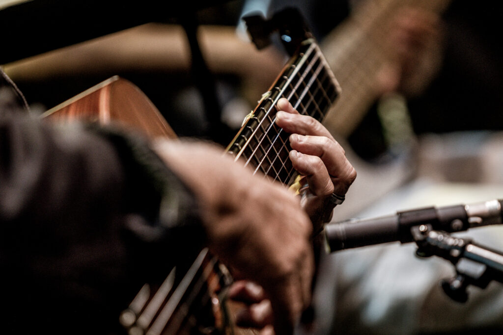 Zdjęcie. Dłonie grające na gitarze akustycznej.