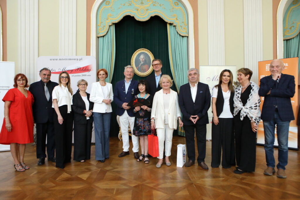 Zdjęcie. Grupa ludzi pozuje do zdjęcia na tle portretu Stanisława Augusta Poniatowskiego.