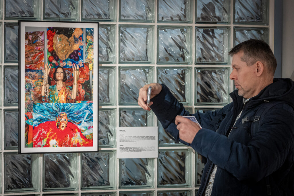 Zdjęcie. Mężczyzna robi zdjęcie telefonem kolorowej fotografii wiszącej w ramce na ścianie.