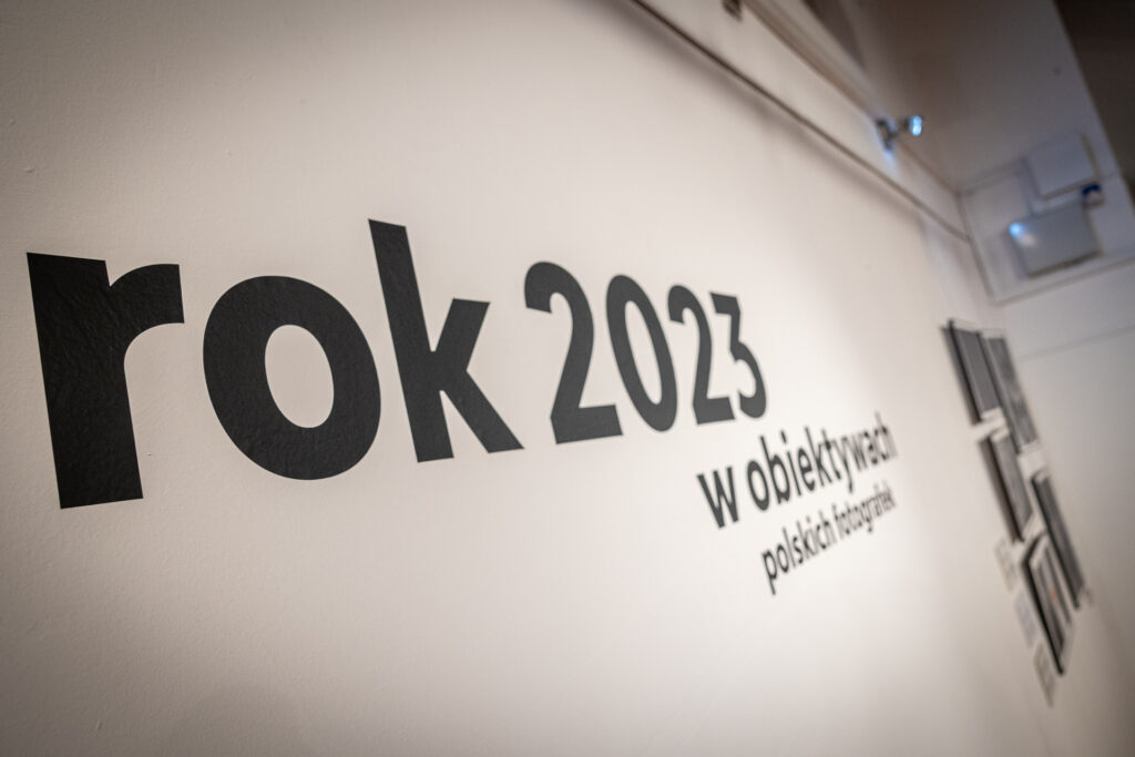 Zdjęcie, Biała ściana z dużym naklejonym napisem: Rok 2023 w obiektywach polskich fotografek.